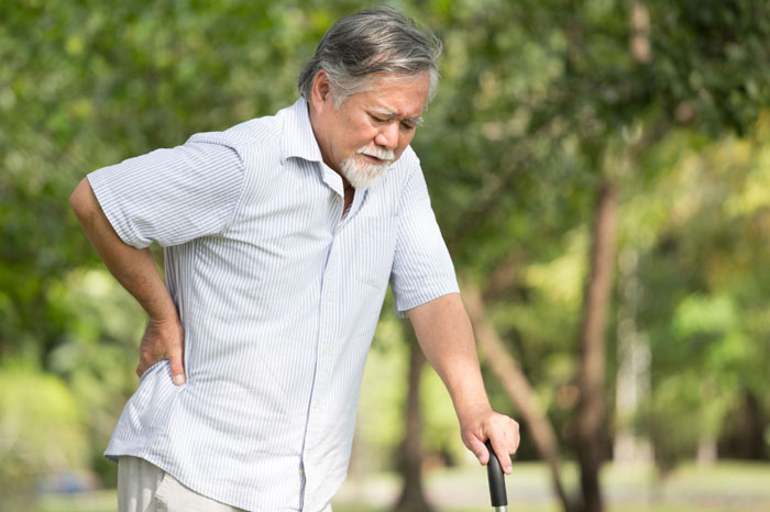 Man struggling with back pain walking with cane